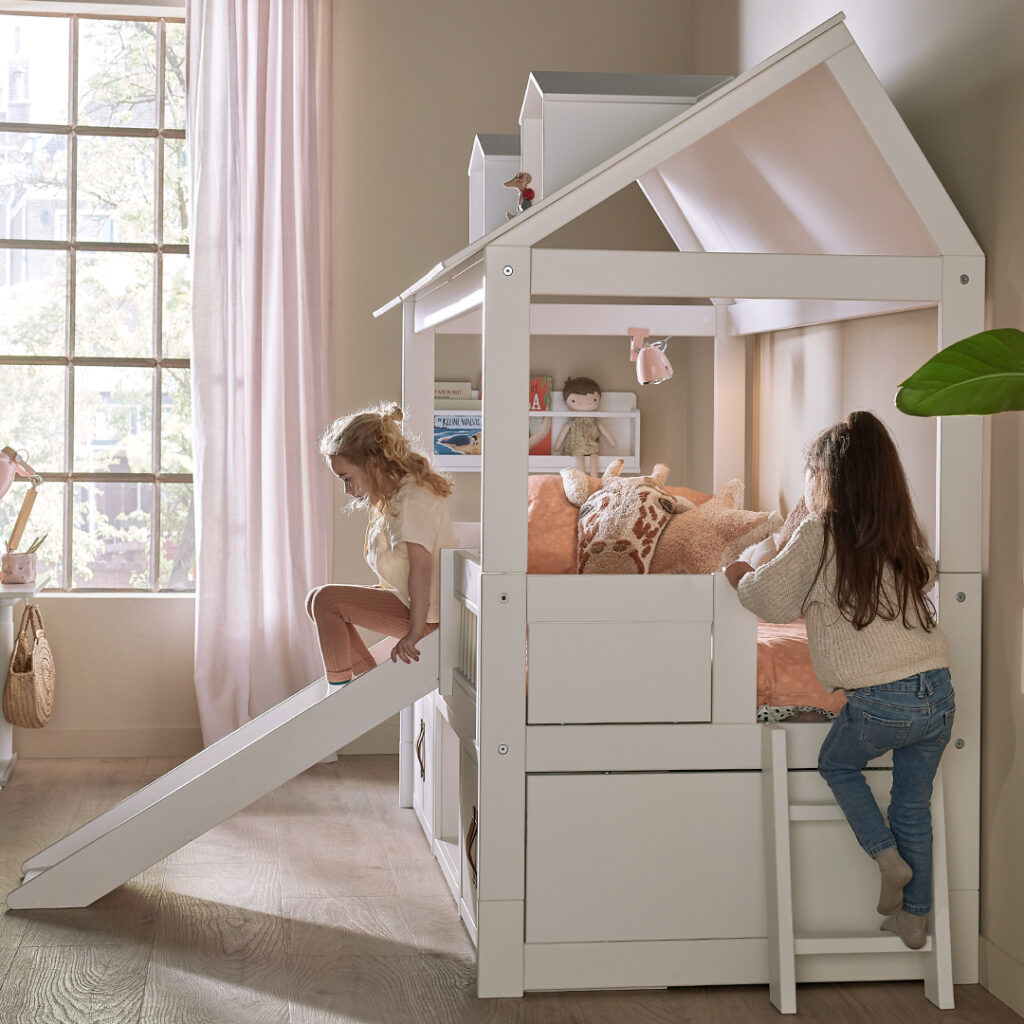 Lit cabane blanc avec toboggan pour enfants, deux filles jouant dedans, chambre lumineuse