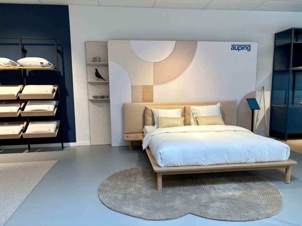 Showroom Auping : lit design en bois avec tête de lit beige, literie blanche et accessoires de décoration modernes