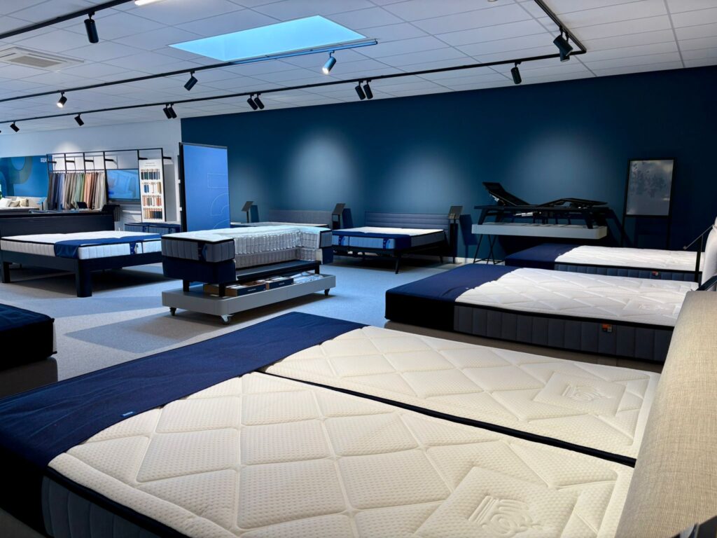 Showroom de matelas avec lits d'exposition, murs bleus, éclairage moderne et diverses marques de literie présentées