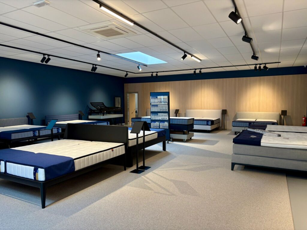 Showroom de matelas avec lits d'exposition, éclairage moderne et design élégant en bleu et bois clair