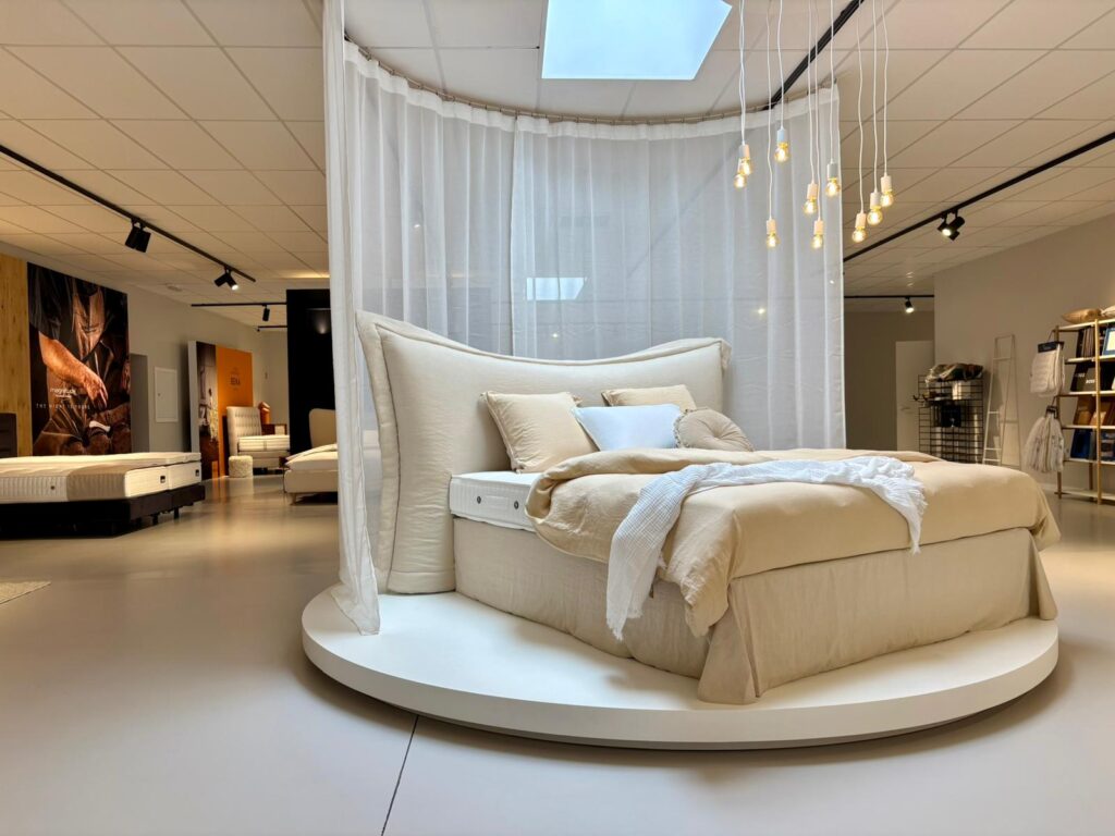 Showroom de lit design avec baldaquin blanc, linge beige et luminaires suspendus modernes
