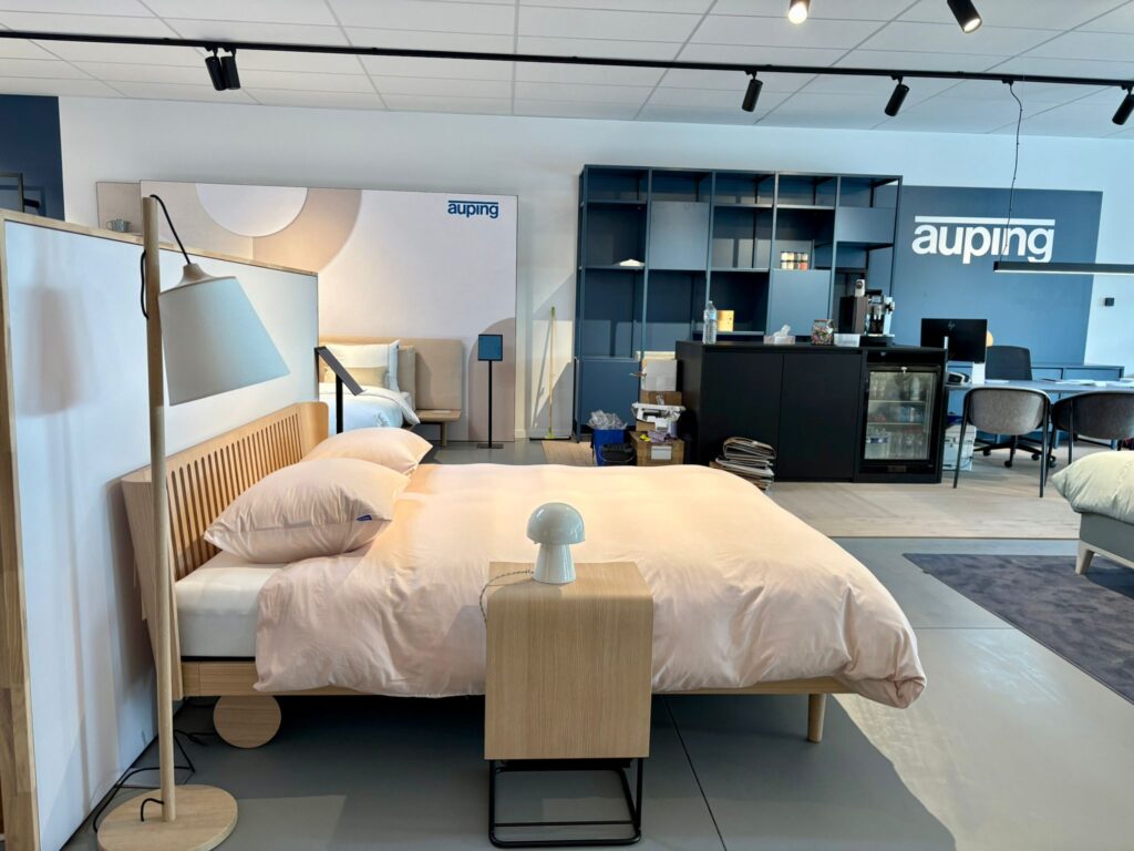 Showroom Auping avec lit design en bois naturel, literie beige et mobilier moderne de chambre à coucher