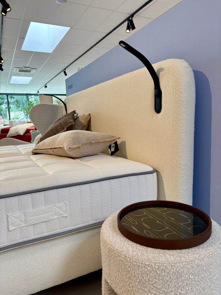 Lit de showroom avec matelas blanc, tête de lit beige et coussins, dans un magasin de literie moderne