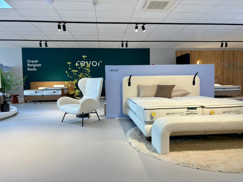 Showroom de lits Revor et Magnitud avec lit AeroPocket, fauteuil blanc et décoration élégante en beige et bleu